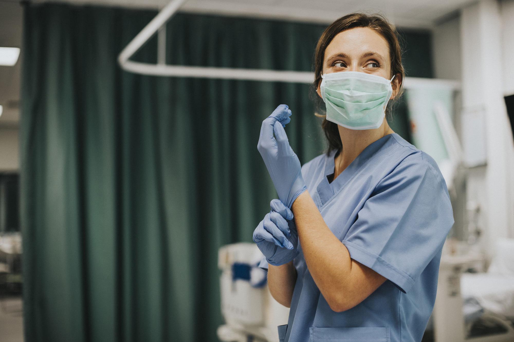 A female registered nurse is putting on medical gloves